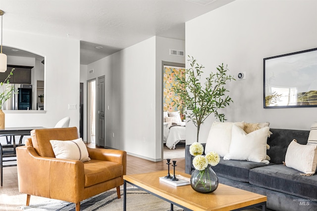 living room with arched walkways, visible vents, baseboards, and wood finished floors