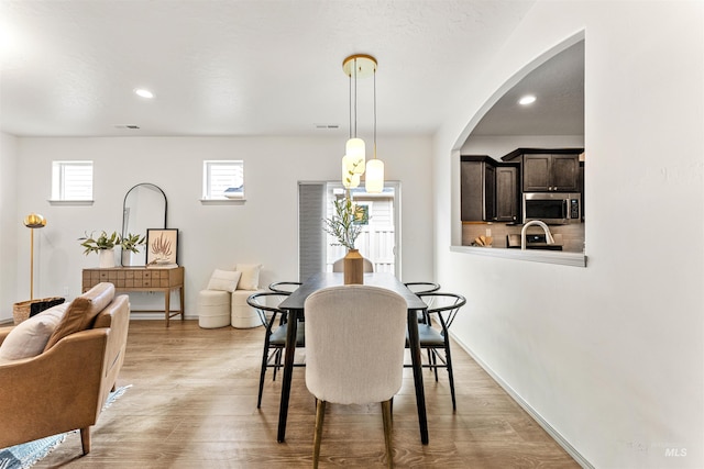 dining space with light wood finished floors, visible vents, baseboards, recessed lighting, and arched walkways