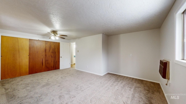 carpeted empty room featuring a textured ceiling, heating unit, and ceiling fan