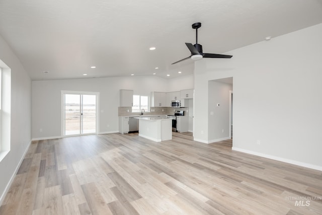 unfurnished living room featuring ceiling fan, lofted ceiling, sink, and light wood-type flooring