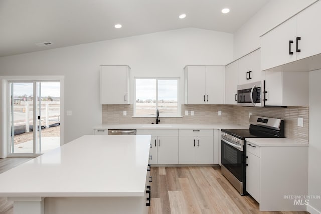 kitchen with white cabinetry, stainless steel appliances, vaulted ceiling, and sink