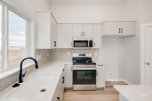 kitchen with sink, white cabinetry, backsplash, stainless steel appliances, and light wood-type flooring