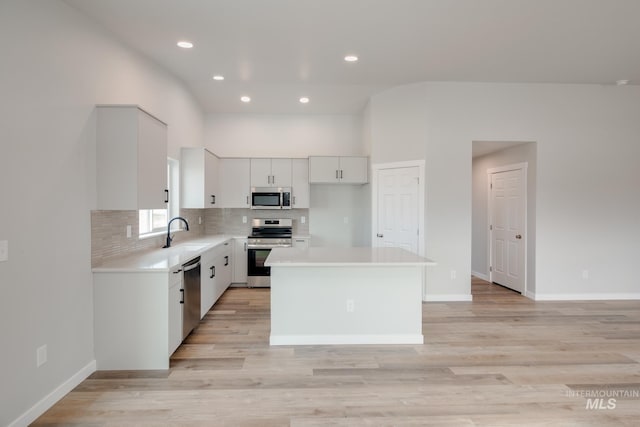 kitchen featuring a kitchen island, white cabinets, stainless steel appliances, light hardwood / wood-style floors, and backsplash