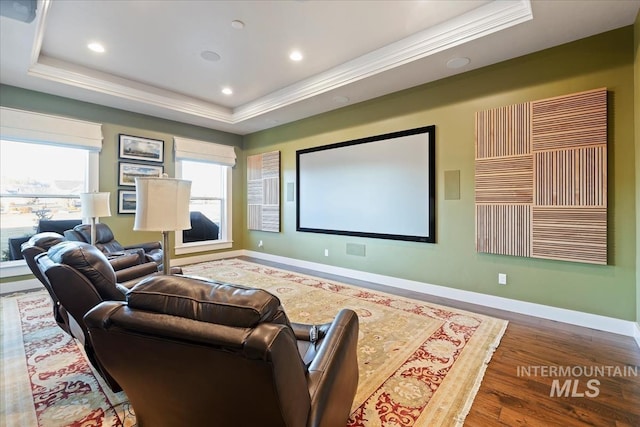 cinema room with hardwood / wood-style floors, a wealth of natural light, and a raised ceiling