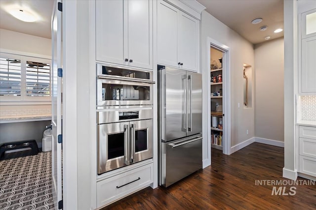 kitchen with dark wood-type flooring, white cabinets, and appliances with stainless steel finishes