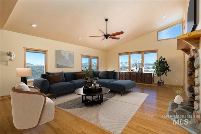 living room featuring light wood-style floors, a ceiling fan, baseboards, and high vaulted ceiling