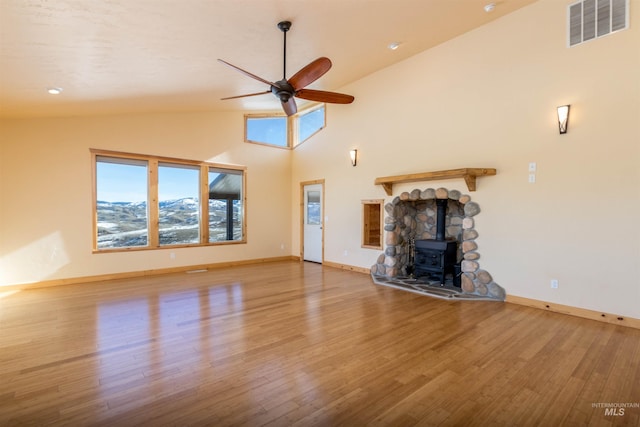 unfurnished living room featuring baseboards, visible vents, a ceiling fan, wood finished floors, and a wood stove