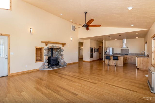 unfurnished living room with arched walkways, baseboards, ceiling fan, light wood-style floors, and high vaulted ceiling