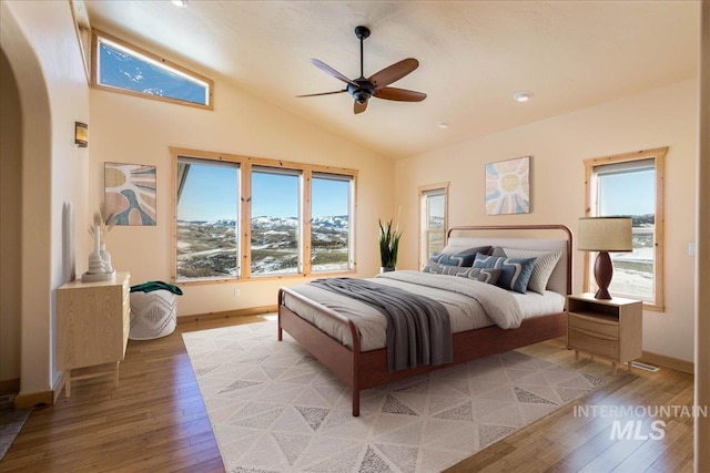 bedroom with light wood-type flooring, arched walkways, multiple windows, and lofted ceiling