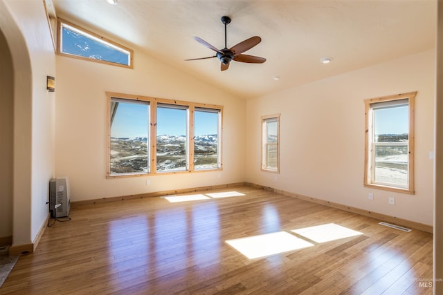 unfurnished room with baseboards, visible vents, arched walkways, lofted ceiling, and wood finished floors