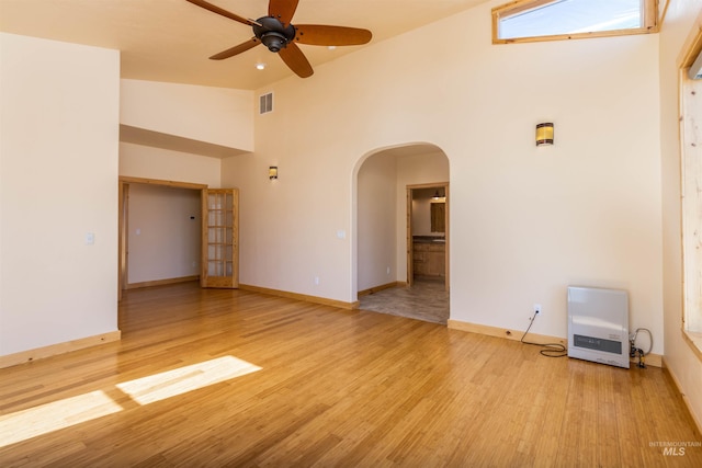 empty room with arched walkways, high vaulted ceiling, visible vents, light wood-type flooring, and heating unit