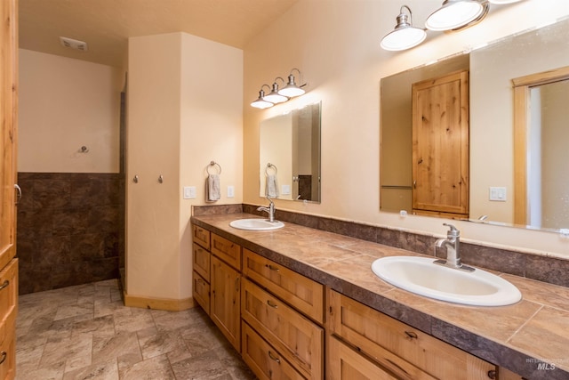 bathroom with stone finish flooring, a sink, baseboards, and double vanity