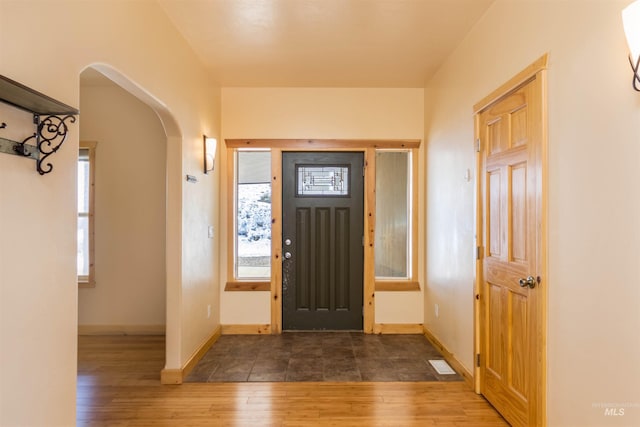 entryway featuring baseboards, arched walkways, and wood finished floors