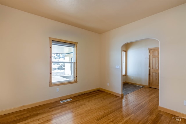 empty room featuring arched walkways, light wood finished floors, visible vents, and baseboards