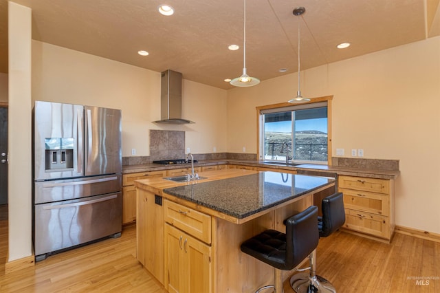 kitchen with light wood-type flooring, wall chimney range hood, stainless steel refrigerator with ice dispenser, and light brown cabinetry