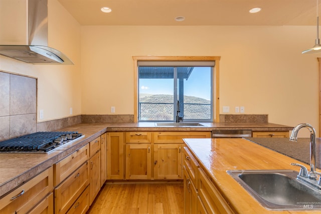 kitchen with dishwasher, stainless steel gas cooktop, wall chimney range hood, and a sink