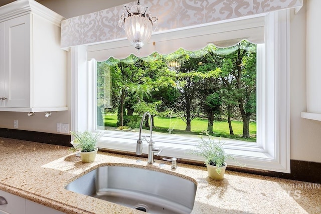 2417 E Brigantine Ct, Eagle, ID 83616 - kitchen view of a sink, light stone countertops, white cabinets, and a chandelier