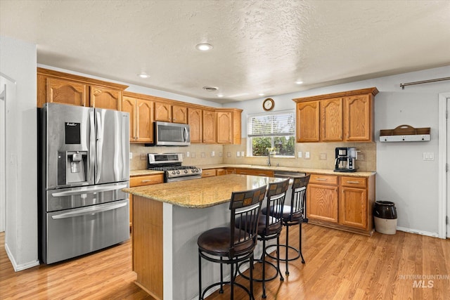 2023 E Wrightwood Dr, Meridian, ID 83642 - kitchen with appliances with stainless steel finishes, decorative backsplash, light wood-style floors, a center island, and brown cabinets