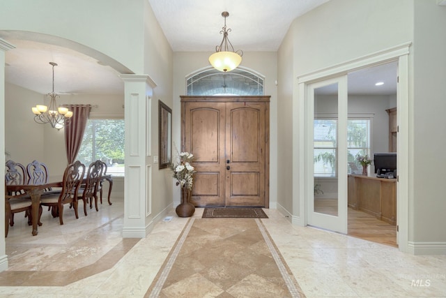 foyer with ornate columns, a notable chandelier, marble finish floor, and baseboards