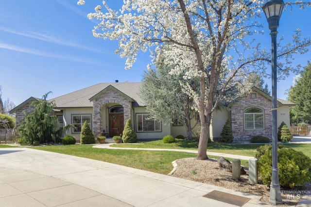 single story home with a shingled roof, stone siding, a front lawn, and stucco siding