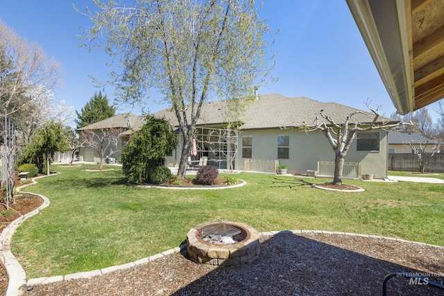 back of property with stucco siding, a lawn, an outdoor fire pit, a patio area, and fence