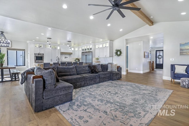 living room with sink, ceiling fan with notable chandelier, light hardwood / wood-style floors, and lofted ceiling with beams