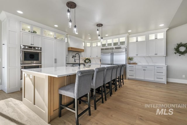 kitchen with premium range hood, a kitchen island with sink, white cabinetry, and appliances with stainless steel finishes