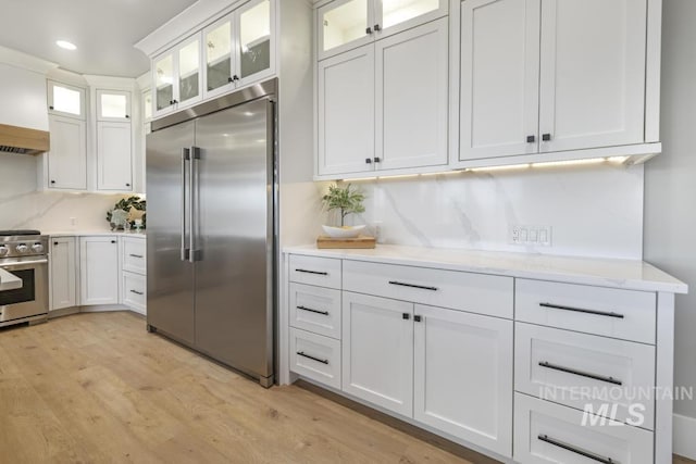 kitchen featuring backsplash, white cabinets, light wood-type flooring, light stone countertops, and high end appliances