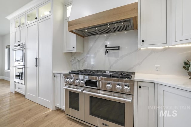 kitchen with light stone countertops, white cabinetry, stainless steel appliances, and custom range hood