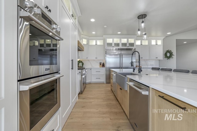 kitchen featuring light stone countertops, white cabinetry, light brown cabinetry, hanging light fixtures, and high quality appliances