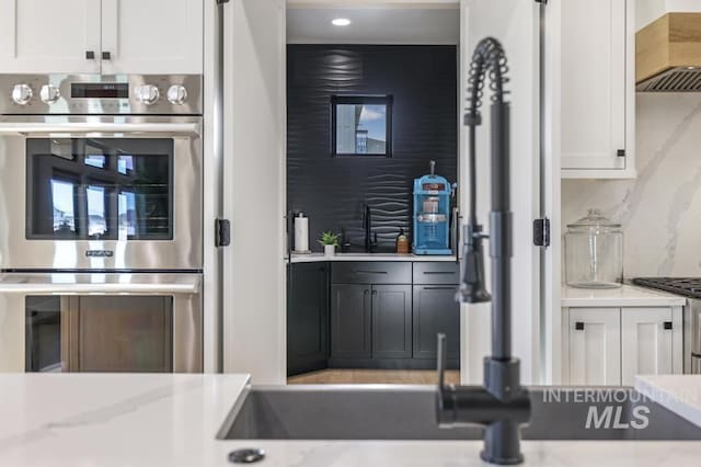 kitchen featuring premium range hood, white cabinetry, stainless steel double oven, and decorative backsplash