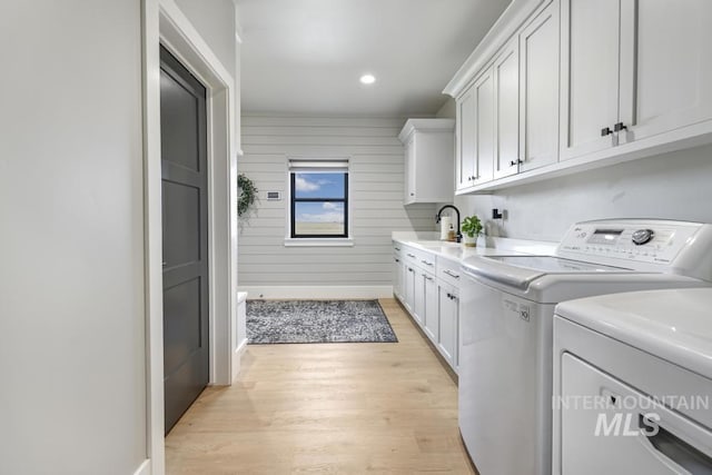 clothes washing area with sink, light hardwood / wood-style flooring, separate washer and dryer, wood walls, and cabinets