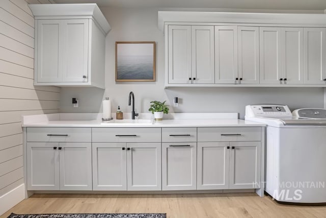 laundry area featuring light hardwood / wood-style floors, washing machine and clothes dryer, sink, wood walls, and cabinets