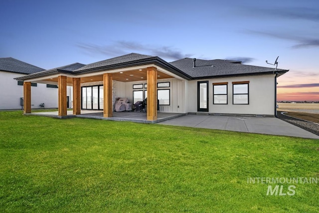 back house at dusk with a lawn and a patio