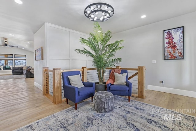 living area featuring light wood-type flooring, ceiling fan with notable chandelier, and lofted ceiling