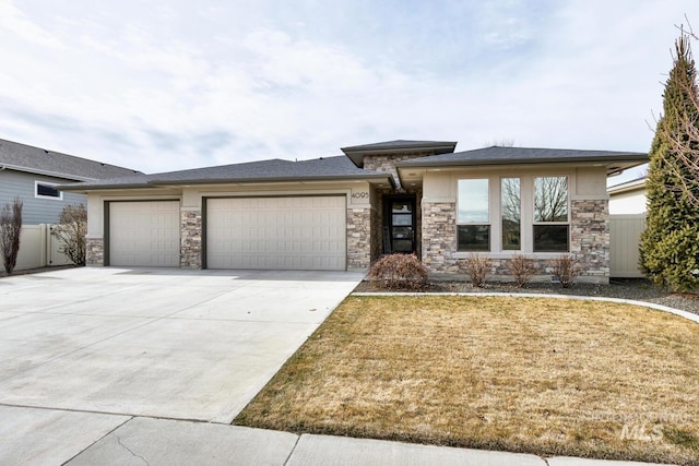 prairie-style home with an attached garage, fence, driveway, stone siding, and a front lawn