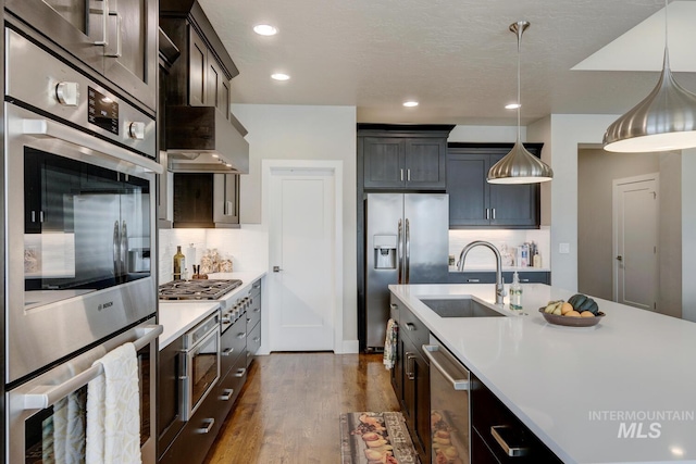 kitchen with dark wood finished floors, stainless steel appliances, light countertops, hanging light fixtures, and a sink