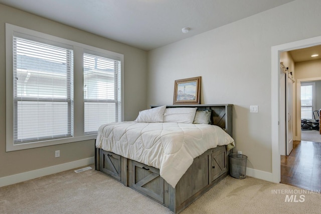 bedroom with a barn door, visible vents, baseboards, and light colored carpet