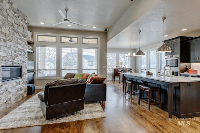 living area with a fireplace, a ceiling fan, a textured ceiling, wood finished floors, and baseboards