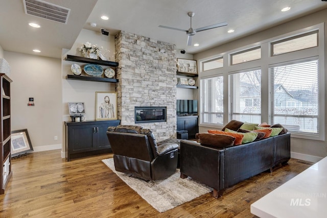 living room with a wealth of natural light, visible vents, a stone fireplace, and wood finished floors