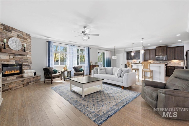 living room featuring crown molding, ceiling fan, light wood-type flooring, and a fireplace