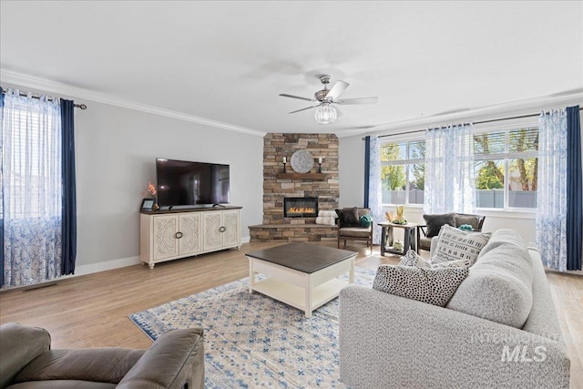 living area with crown molding, baseboards, a stone fireplace, ceiling fan, and light wood-style flooring