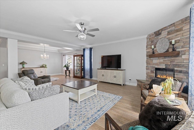 living room featuring crown molding, a stone fireplace, ceiling fan with notable chandelier, baseboards, and wood finished floors
