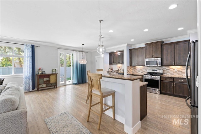 kitchen featuring crown molding, dark brown cabinets, open floor plan, a kitchen breakfast bar, and appliances with stainless steel finishes