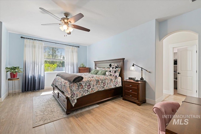 bedroom featuring arched walkways, baseboards, a ceiling fan, and light wood-style flooring