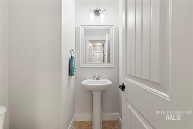 half bath featuring toilet, baseboards, and a sink