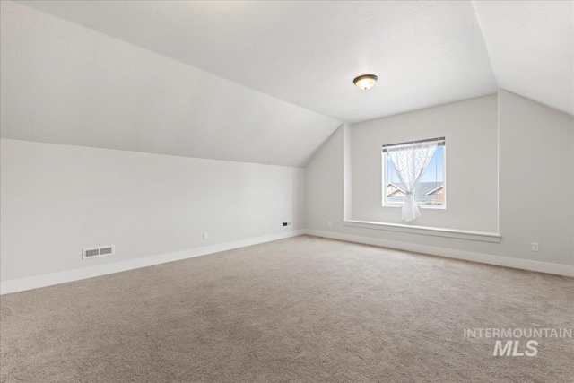 additional living space with baseboards, carpet flooring, vaulted ceiling, and visible vents