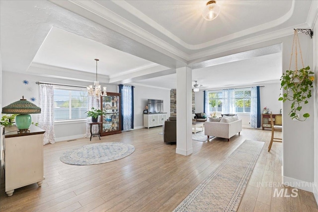 foyer entrance featuring a notable chandelier, light wood-style floors, baseboards, a tray ceiling, and ornamental molding