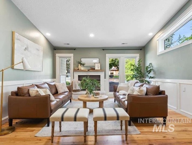 1803 E Danmor Dr, Boise, ID 83712 - living room featuring light wood-type flooring, a decorative wall, a brick fireplace, a wainscoted wall, and a textured ceiling