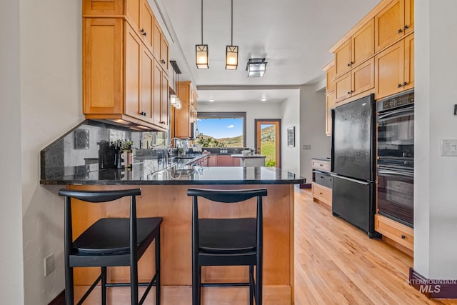 4997 N Brookside Ln, Boise, ID 83714 - kitchen with black appliances, a peninsula, light wood-type flooring, dark countertops, and a kitchen bar